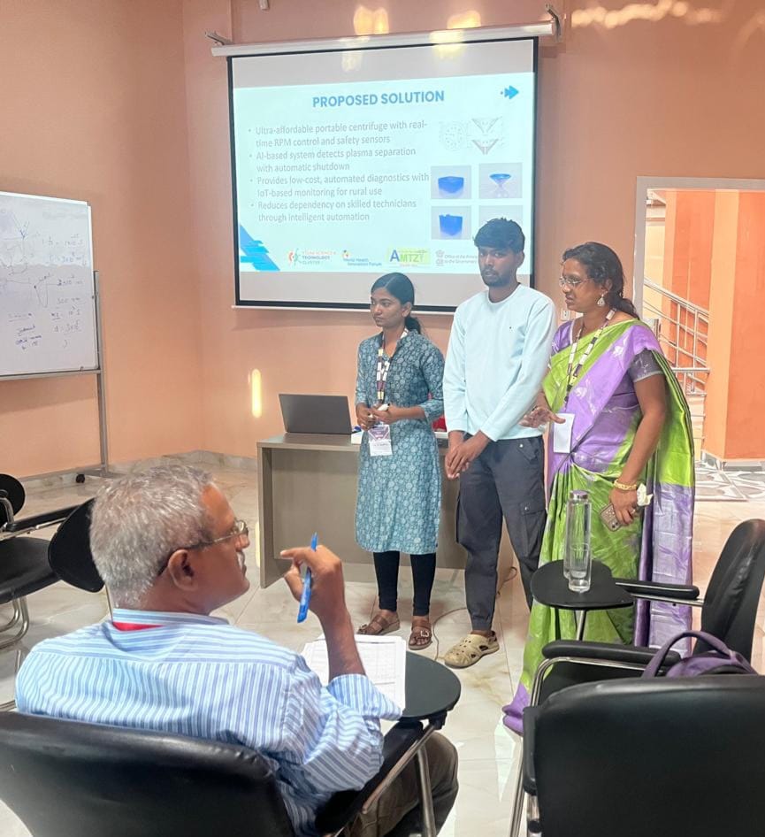 Team members presenting their proposed solution — an ultra-affordable portable centrifuge with AI-based plasma separation detection and IoT monitoring — to a reviewer.